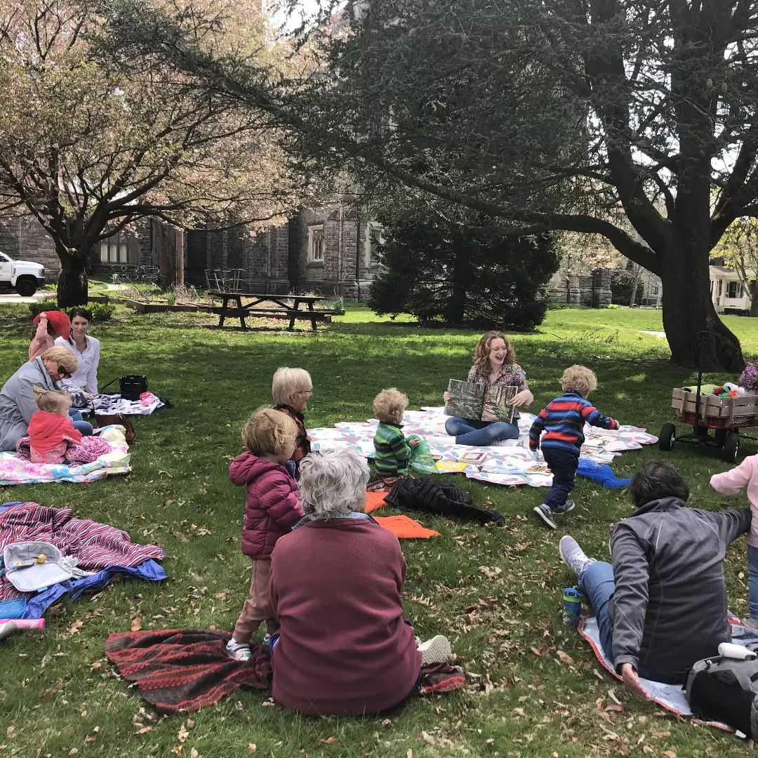 Children's Librarian Allie reads to kids and families on a blanket during outdoor stroytime in early spring.