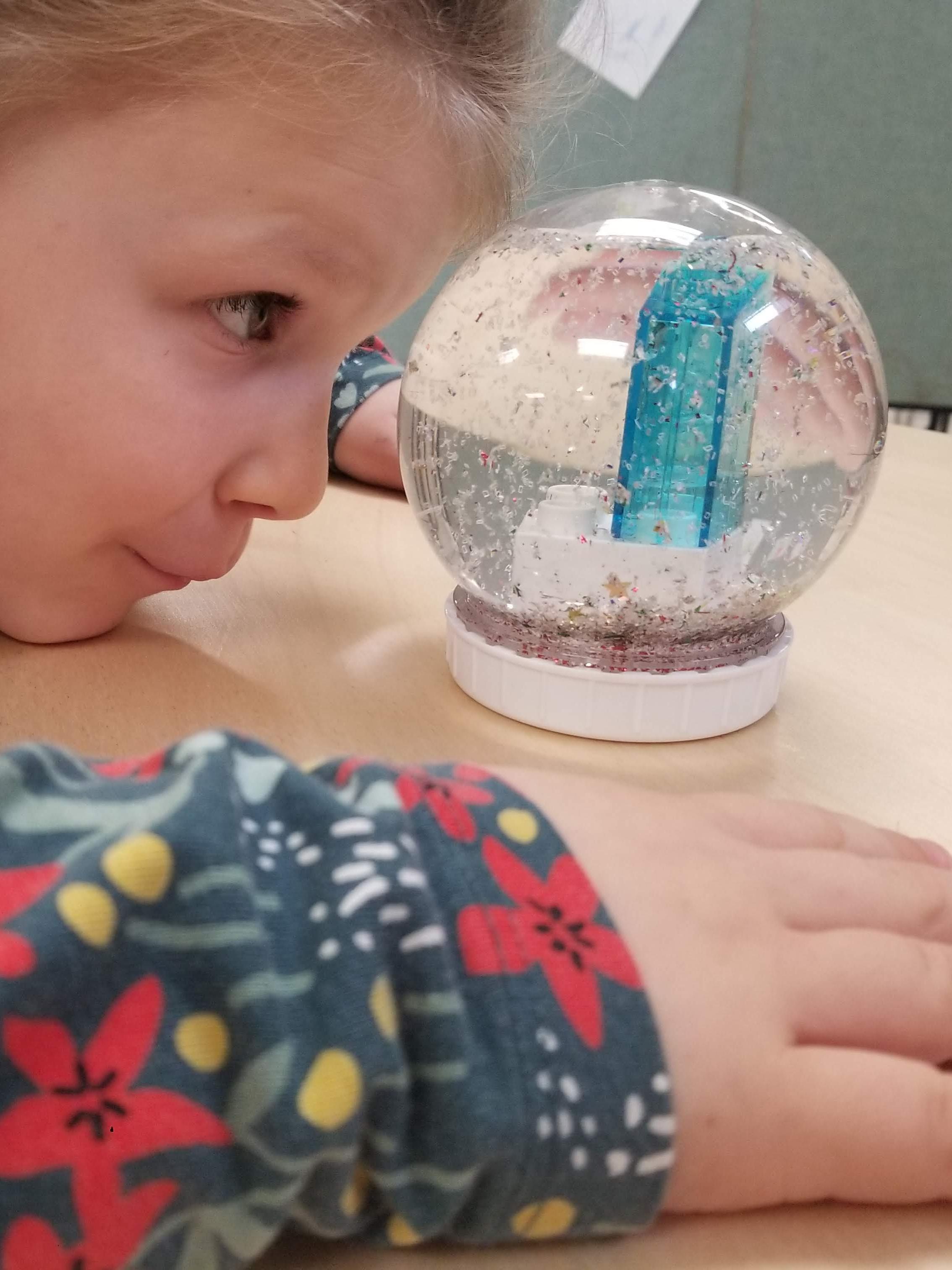 A Pre-k storytime kid marvels at her creation: a snow globe filled with sparkly glitter and a repurposed Duplo brick!