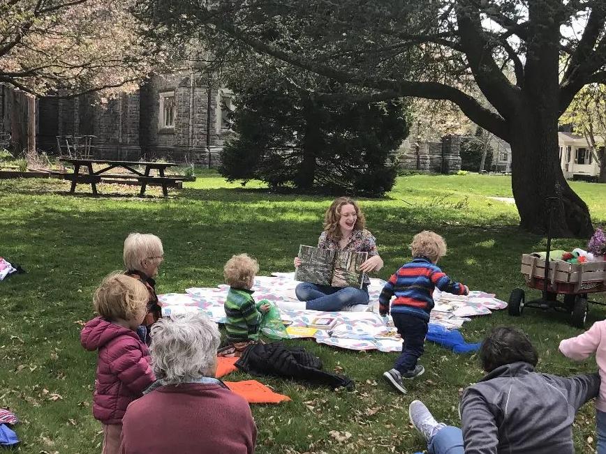 Children's Librarian Allie reads to kids and families on a blanket during outdoor stroytime in early spring.